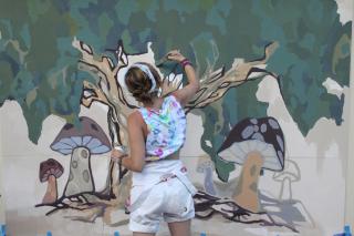 Artist painting mural entitled Shady Tree Maker