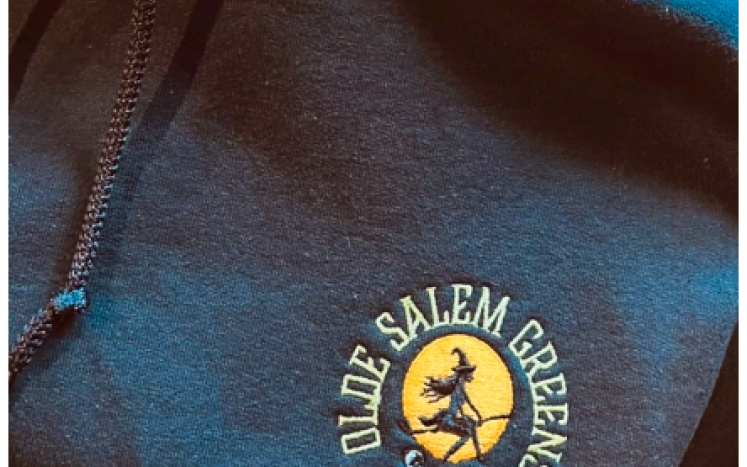 Logo on a sweatshirt of a witch riding a golf club like a broomstick